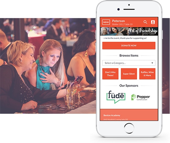 Two women at an event using event fundraising software with a mobile phone showcasing the mobile bidding user interface overlayed